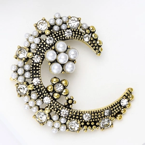 Détail d'une broche demi-lune vintage avec perles et strass sur base en alliage doré