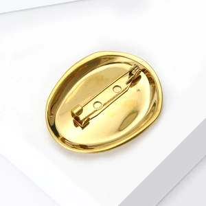 Golden oval stainless steel brooch with secure pin back on minimalist white pedestal