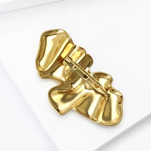 Artistic gold irregular wavy brooch with back pin clasp on a minimalist white stage