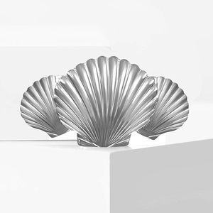 Three linked scallop shell brooches in polished silver stainless steel on a white pedestal