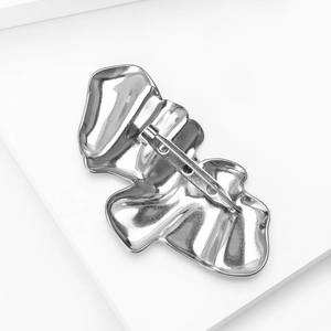 Macro shot of silver wavy brooch back featuring a secure metal pin and polished texture