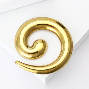 Close-up of a polished gold spiral snail-shaped brooch on a white minimalist block