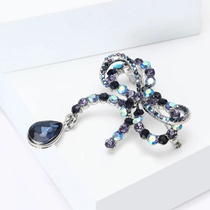 Close-up of vintage bow brooch with multicolored crystals and blue teardrop pendant
