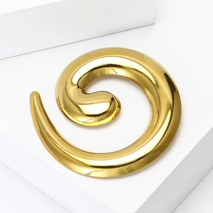 Macro shot of a high-polished golden spiral brooch on a minimalist white display