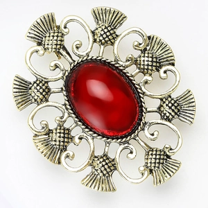 Détail d'une broche chardon vintage avec grand cabochon rouge et motifs en filigrane