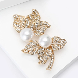 Détail d'une broche feuille avec perles blanches et strass brillants sur base dorée