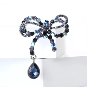 Vintage crystal bow brooch with blue teardrop pendant on a white geometric stand