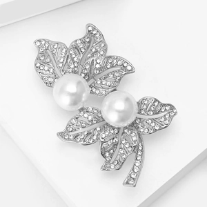 Gros plan d'une broche feuille argentée ornée de cristaux et de deux perles blanches
