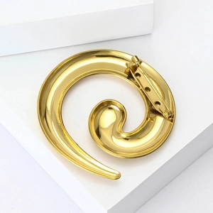 Minimalist golden spiral snail brooch with polished finish on a white podium