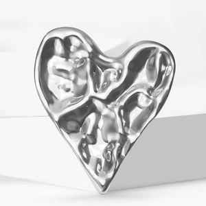 Modern silver heart brooch with textured lava design on a geometric white display stand