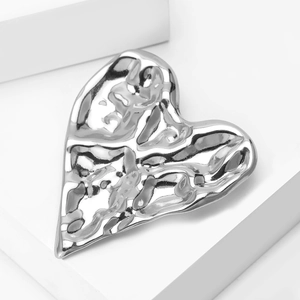 Macro shot of silver heart brooch with liquid metal texture on white geometric steps