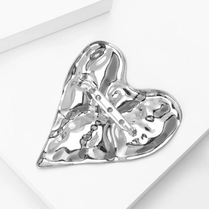 Macro view of a silver heart brooch with hammer-textured surface and metallic finish
