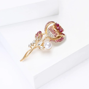 Détail d'une broche en forme de rose avec strass roses et perle blanche sur métal doré