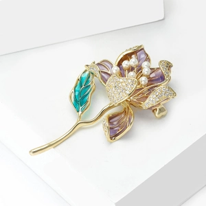 Détail de la broche fleur en émail vert et pétales violets avec strass et perles blanches