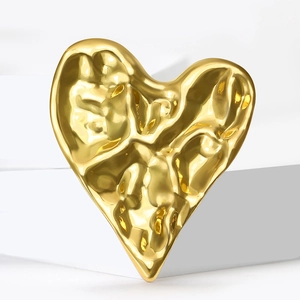 Macro shot of gold heart-shaped brooch with textured hammered metal finish and reflections