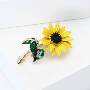 Dettaglio della spilla a girasole in smalto giallo con foglie verdi su supporto bianco