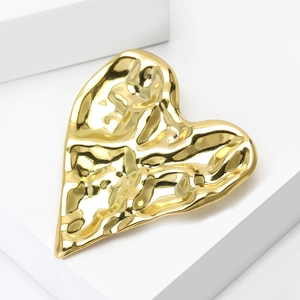 Macro shot of gold heart brooch with hammered wave texture on minimalist white pedestal