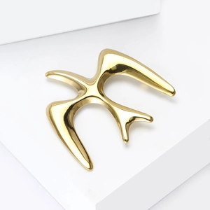 Detailed view of flying swallow brooch in polished gold finish on white pedestal