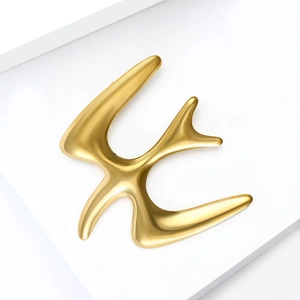Detailed view of elegant gold swallow brooch with matte finish on white geometric stand