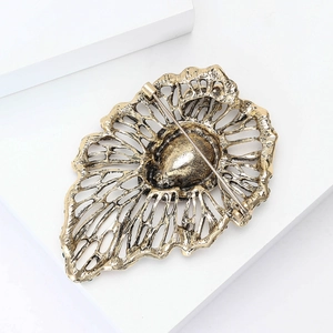 Vintage hollowed-out gold brooch with intricate leaf texture and pin back mechanism
