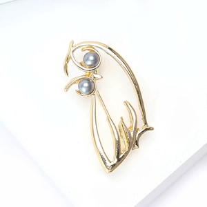 Détail de broche hibou dorée ajourée avec perles grises élégantes et finition lisse