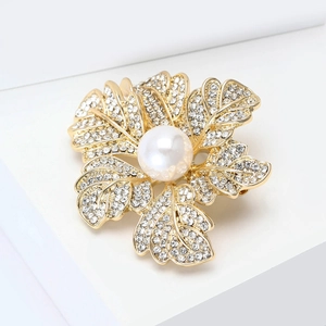 Détail d'une broche dorée avec une grande perle et des motifs de feuilles brillants