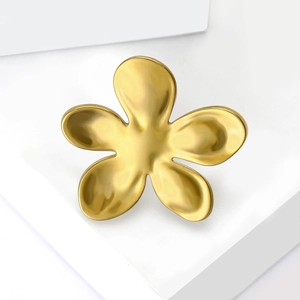 Macro view of matte golden flower brooch with brushed metal finish on white pedestal