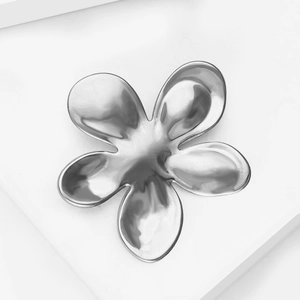 Detail of liquid metal flower brooch with polished silver mirror finish on white pedestal