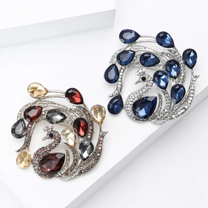 Elegant rhinestone peacock brooches in blue and burgundy on a white geometric stand