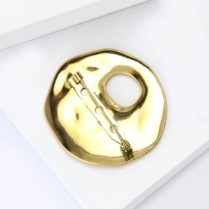 Macro shot of gold liquid metal brooch back with secure pin on white geometric block