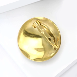 Golden liquid metal textured round brooch with hammer finish on a minimalist background