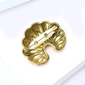 Polished gold stainless steel shell brooch with secure pin closure on white display