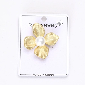 Detailed close-up of a gold floral alloy brooch with elegant white pearl on a white card