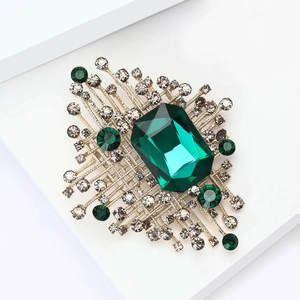 Dettaglio spilla con smeraldo verde e strass grigi su una base in lega dorata di lusso