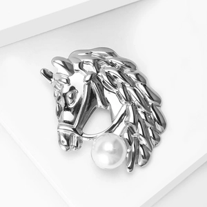 Macro detail of silver horse head brooch with polished metal and a large round white pearl