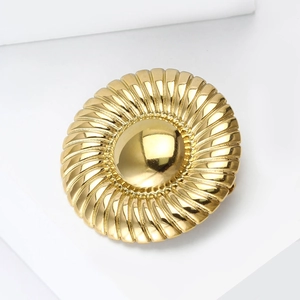 Polished gold sunburst brooch pin with spiral texture on minimalist white background