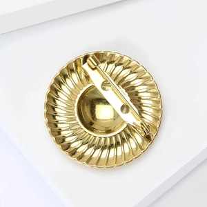 Macro shot of the gold brooch back view showing safety pin clasp and textured metal edges