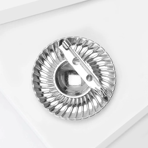 Polished stainless steel round brooch with textured sunburst pattern and safety pin back