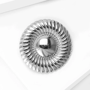 Macro view of silver round brooch with radial spiral texture and center bead detail