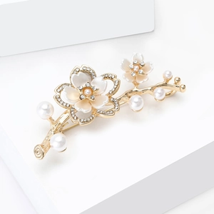 Dettaglio spilla a fiore dorato con petali di madreperla bianca e strass scintillanti