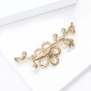 Elegante spilla a fiore di pesco dorata con perle bianche e strass su piedistallo bianco