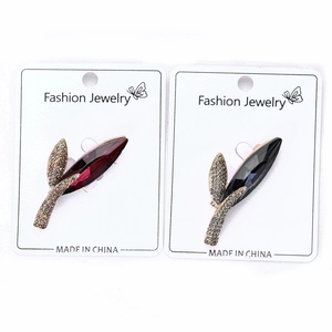 Detailed view of elegant leaf brooches with red and blue crystals on display card