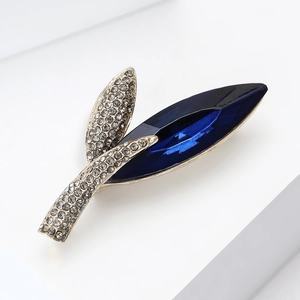 Detailed close-up of leaf brooch featuring a large blue marquise crystal and grey diamonds
