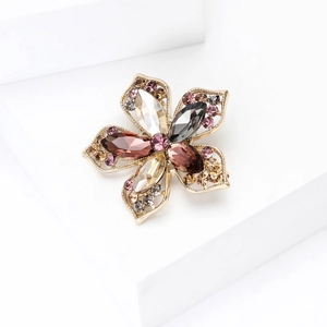 Détail de la broche fleur avec strass colorés sur un présentoir blanc minimaliste
