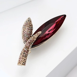 Detailed macro view of a gold-plated leaf brooch with a deep red marquise gemstone and rhinestones