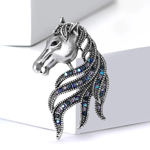 Vintage silver horse head brooch with blue and purple crystals on a white pedestal