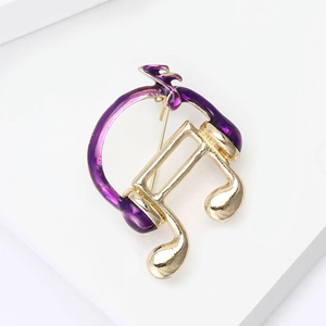 Macro shot of musical headphone brooch in purple and gold on a white geometric stand