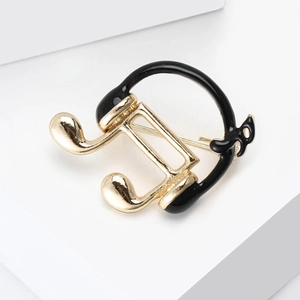 Close-up of music note and headphones brooch with golden finish and black enamel detail