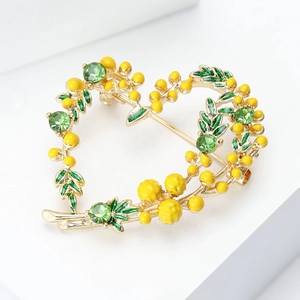 Détail d'une broche cœur dorée avec bourgeons jaunes et feuilles en cristal vert