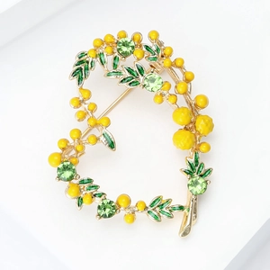 Détail d'une broche en forme de cœur avec fleurs de mimosa jaunes et feuilles en émail